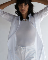 Close-up of a female model wearing the Annette Poplin Shirt layered over a white tank top and white jeans. 