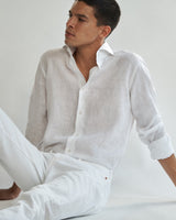 Seated male model wearing the white Pearson Linen Shirt and white jeans.